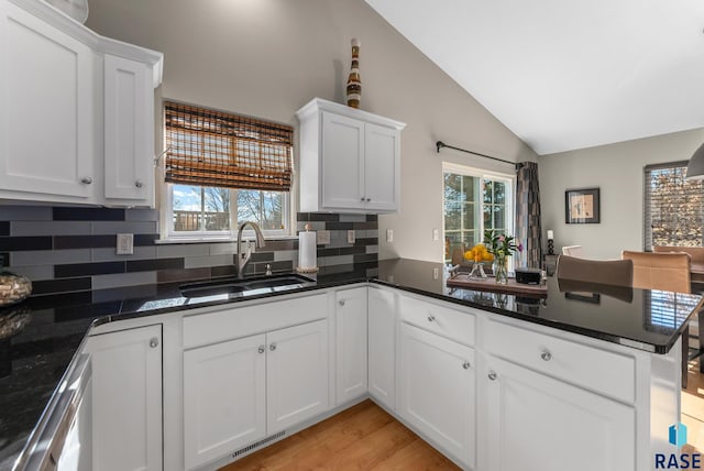 kitchen featuring vaulted ceiling, sink, white cabinets, and kitchen peninsula