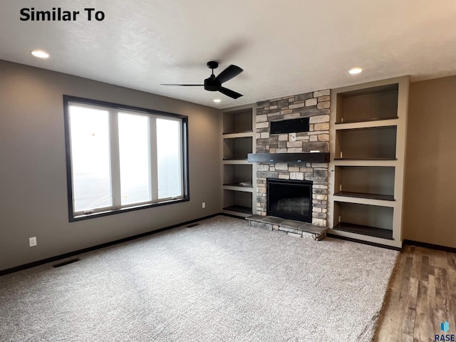 unfurnished living room with a stone fireplace, built in features, ceiling fan, and hardwood / wood-style flooring