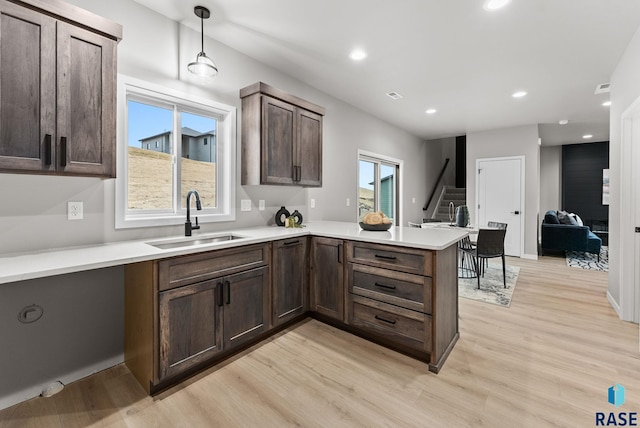 kitchen with pendant lighting, sink, dark brown cabinetry, kitchen peninsula, and light hardwood / wood-style flooring