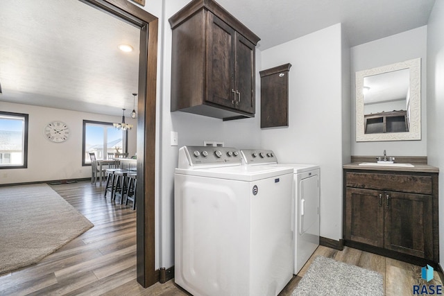 clothes washing area with sink, cabinets, a chandelier, washer and dryer, and light wood-type flooring