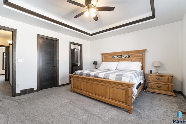 bedroom with ensuite bath, light carpet, ceiling fan, and a tray ceiling