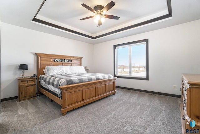 carpeted bedroom featuring ceiling fan and a raised ceiling