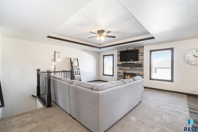 living room featuring a tray ceiling, a stone fireplace, and a wealth of natural light