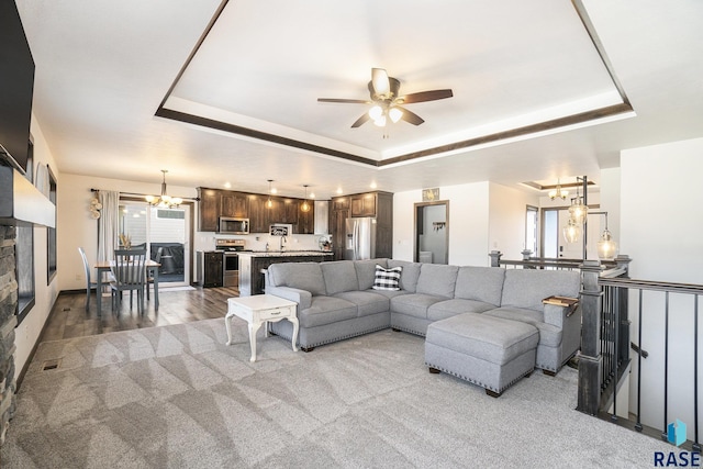 living room featuring a raised ceiling, plenty of natural light, and ceiling fan with notable chandelier