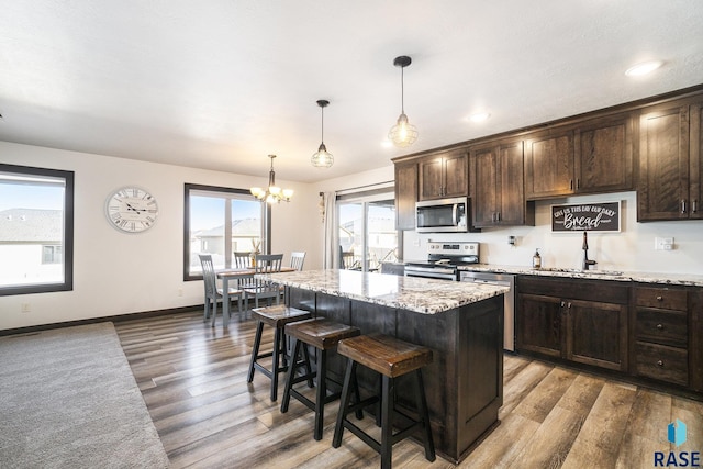 kitchen featuring a kitchen island, appliances with stainless steel finishes, sink, dark brown cabinetry, and light stone countertops