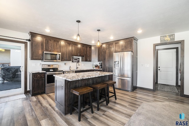 kitchen featuring hanging light fixtures, a center island, stainless steel appliances, dark brown cabinets, and light wood-type flooring