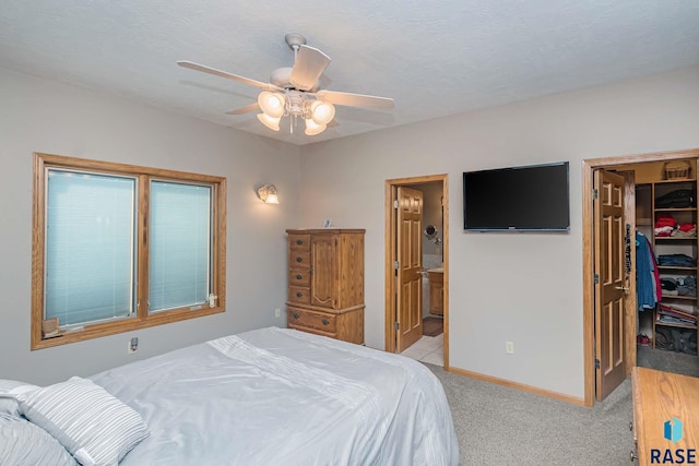 bedroom featuring ceiling fan, connected bathroom, a walk in closet, light colored carpet, and a closet