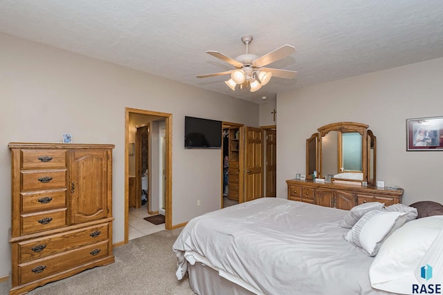 bedroom with ceiling fan, a spacious closet, light colored carpet, and a textured ceiling