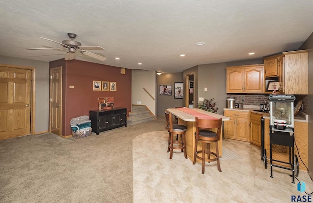 kitchen with a breakfast bar, tasteful backsplash, a textured ceiling, ceiling fan, and light colored carpet