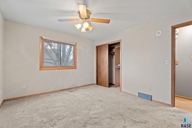 unfurnished bedroom featuring ceiling fan, light colored carpet, a textured ceiling, and a closet