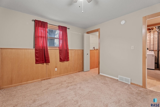 carpeted empty room featuring washer / clothes dryer, a textured ceiling, and wooden walls