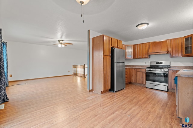 kitchen featuring custom exhaust hood, ceiling fan, light hardwood / wood-style floors, stainless steel appliances, and a textured ceiling