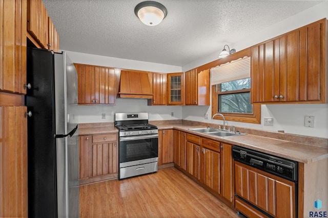 kitchen with sink, appliances with stainless steel finishes, premium range hood, light hardwood / wood-style floors, and a textured ceiling