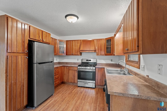 kitchen with appliances with stainless steel finishes, sink, light hardwood / wood-style floors, a textured ceiling, and wall chimney exhaust hood