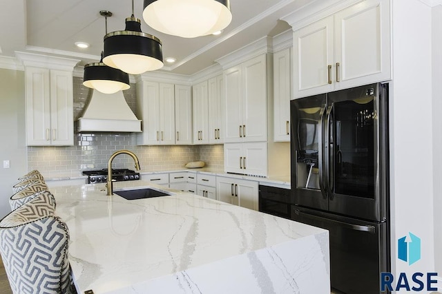 kitchen with sink, white cabinetry, hanging light fixtures, light stone counters, and black fridge