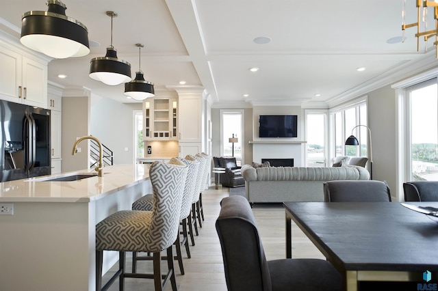 dining area with coffered ceiling, ornamental molding, sink, and light hardwood / wood-style floors