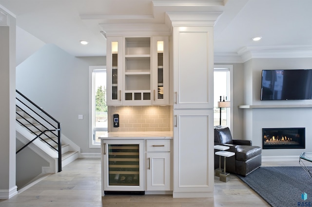 bar featuring wine cooler, white cabinetry, ornamental molding, and light hardwood / wood-style floors