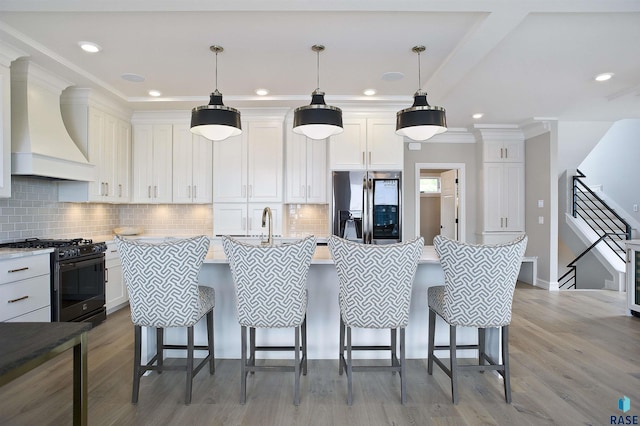 kitchen with decorative light fixtures, a kitchen bar, stainless steel fridge with ice dispenser, black gas stove, and wall chimney exhaust hood