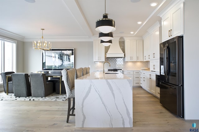 kitchen with black fridge, custom range hood, white cabinets, and light stone counters