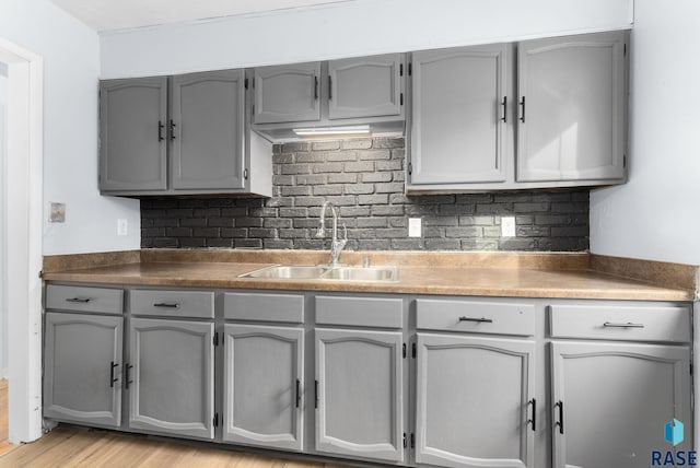 kitchen featuring decorative backsplash, sink, light hardwood / wood-style flooring, and gray cabinetry