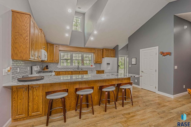 kitchen with white appliances, a kitchen breakfast bar, light hardwood / wood-style floors, light stone countertops, and kitchen peninsula