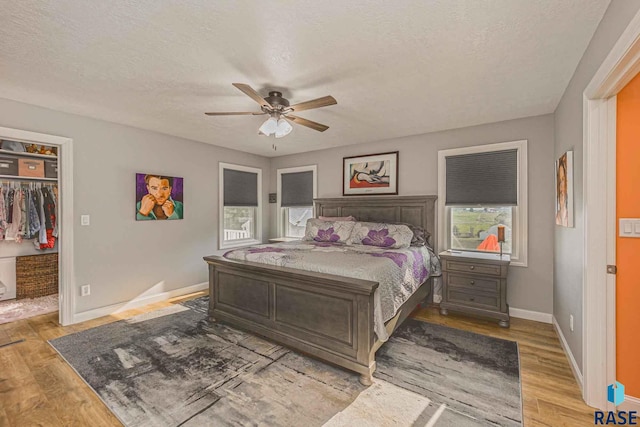 bedroom with ceiling fan, a walk in closet, a textured ceiling, and light wood-type flooring