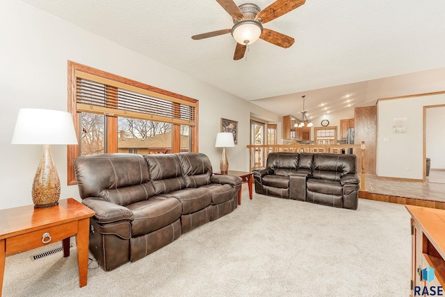 carpeted living room featuring ceiling fan with notable chandelier, vaulted ceiling, and a textured ceiling