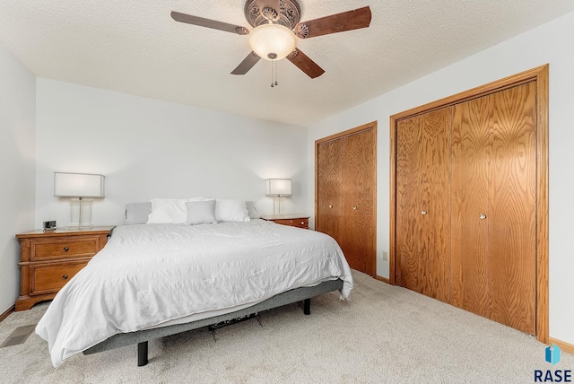 bedroom featuring ceiling fan, a textured ceiling, light colored carpet, and multiple closets