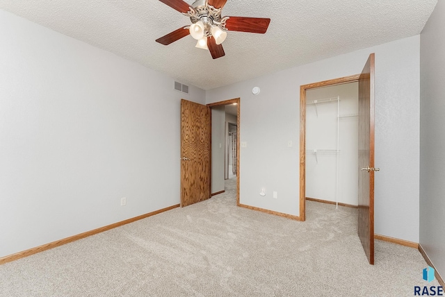 unfurnished bedroom with a walk in closet, light carpet, a textured ceiling, a closet, and ceiling fan