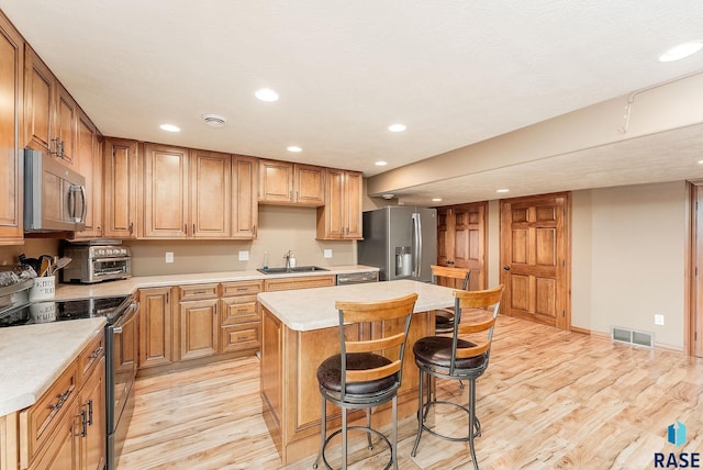 kitchen featuring a breakfast bar, sink, a center island, light hardwood / wood-style flooring, and stainless steel appliances