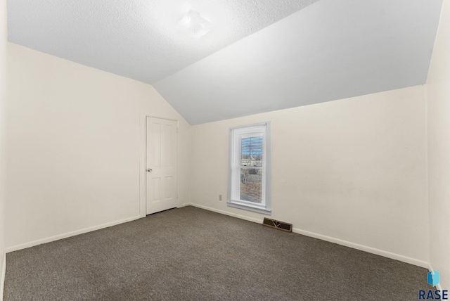 additional living space featuring lofted ceiling, a textured ceiling, and dark colored carpet