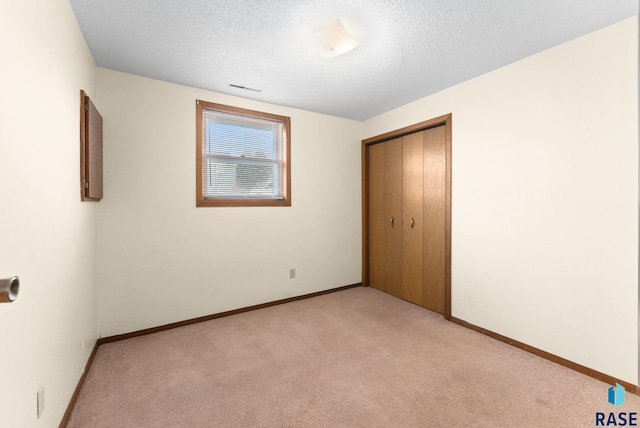 unfurnished bedroom featuring light carpet, a textured ceiling, and a closet