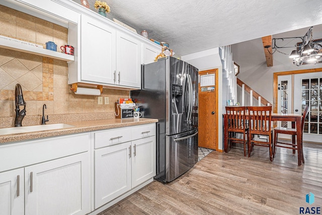 kitchen with sink, white cabinets, decorative backsplash, stainless steel refrigerator with ice dispenser, and light hardwood / wood-style flooring