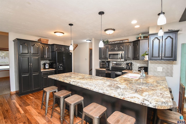 kitchen with sink, a kitchen breakfast bar, kitchen peninsula, pendant lighting, and stainless steel appliances