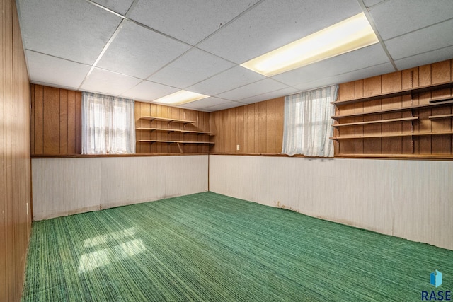 basement with carpet flooring, a paneled ceiling, and wooden walls