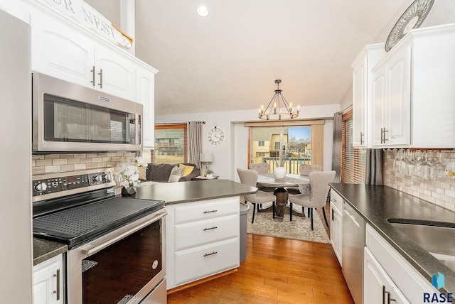 kitchen featuring white cabinetry, appliances with stainless steel finishes, decorative light fixtures, and light wood-type flooring