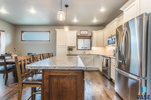 kitchen featuring a kitchen island, appliances with stainless steel finishes, pendant lighting, sink, and dark wood-type flooring