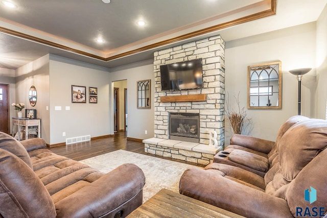 living room featuring dark hardwood / wood-style flooring, a stone fireplace, ornamental molding, and a raised ceiling