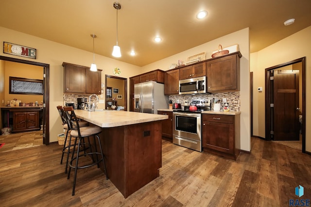 kitchen with appliances with stainless steel finishes, decorative light fixtures, backsplash, dark hardwood / wood-style flooring, and dark brown cabinets