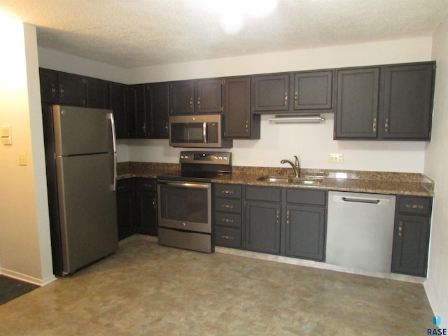 kitchen with stainless steel appliances, sink, a textured ceiling, and dark stone counters