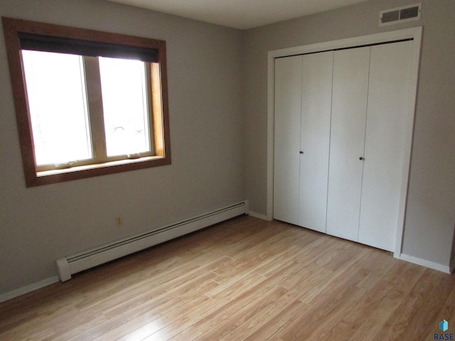 unfurnished bedroom with light hardwood / wood-style flooring, a closet, and baseboard heating