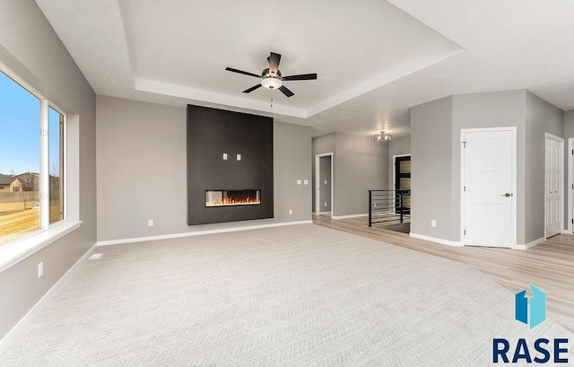 unfurnished living room with a tray ceiling, light hardwood / wood-style floors, a large fireplace, and ceiling fan