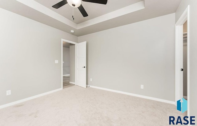 carpeted empty room with a raised ceiling and ceiling fan