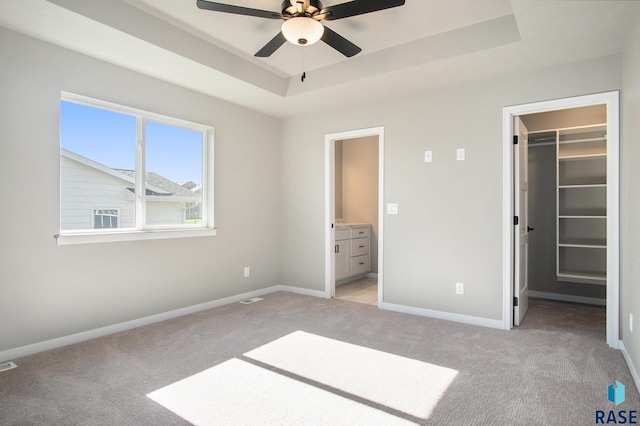 unfurnished bedroom featuring a closet, a walk in closet, light colored carpet, and a raised ceiling