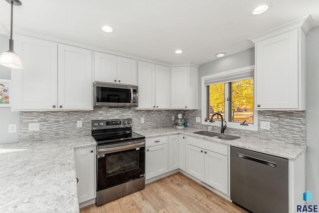 kitchen with sink, white cabinetry, light stone counters, decorative light fixtures, and appliances with stainless steel finishes