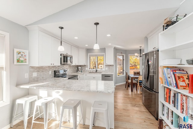 kitchen with appliances with stainless steel finishes, sink, white cabinets, a kitchen bar, and kitchen peninsula