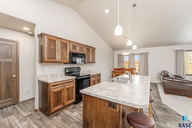 kitchen with a breakfast bar, sink, hanging light fixtures, an island with sink, and black appliances