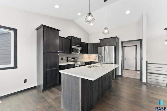 kitchen with sink, hanging light fixtures, stainless steel appliances, light stone countertops, and an island with sink