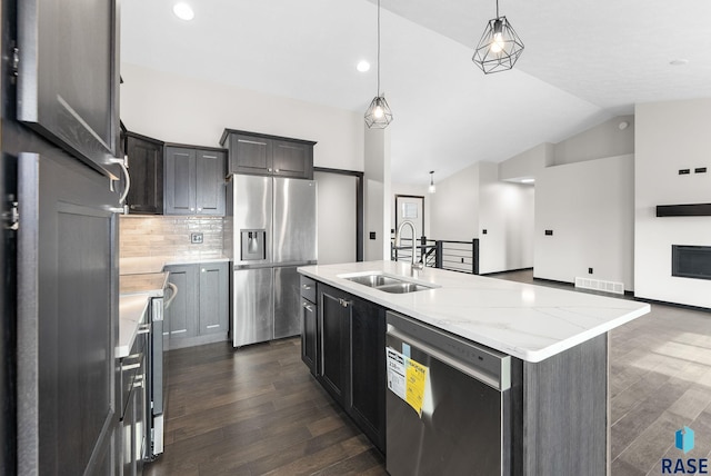 kitchen with pendant lighting, lofted ceiling, sink, a kitchen island with sink, and stainless steel appliances