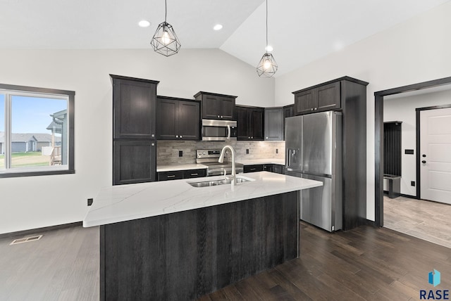 kitchen featuring sink, light stone counters, decorative light fixtures, stainless steel appliances, and a kitchen island with sink